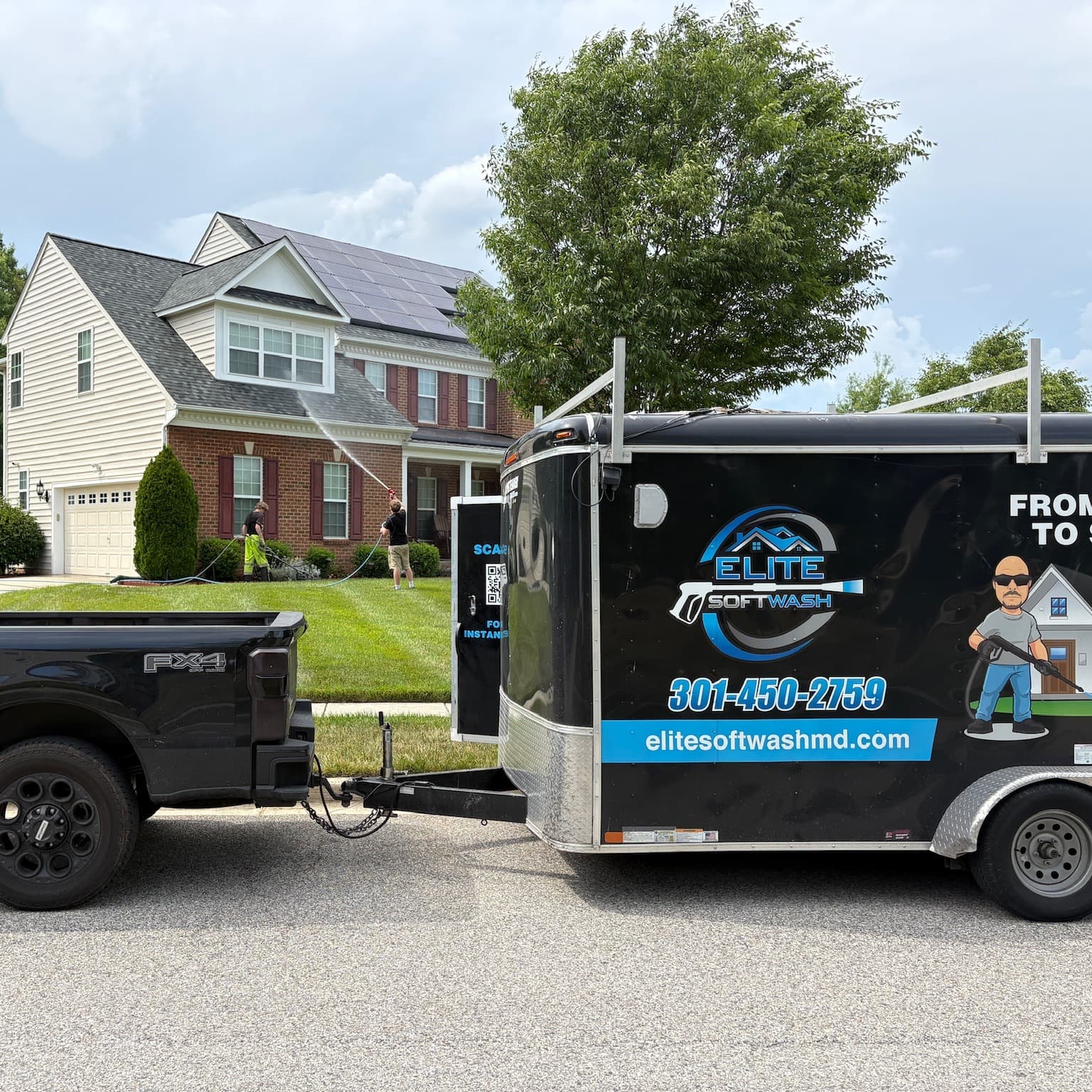 Elite Soft Wash crew soft washing a brick and vinyl home in Maryland, with the branded truck and trailer parked at the curb